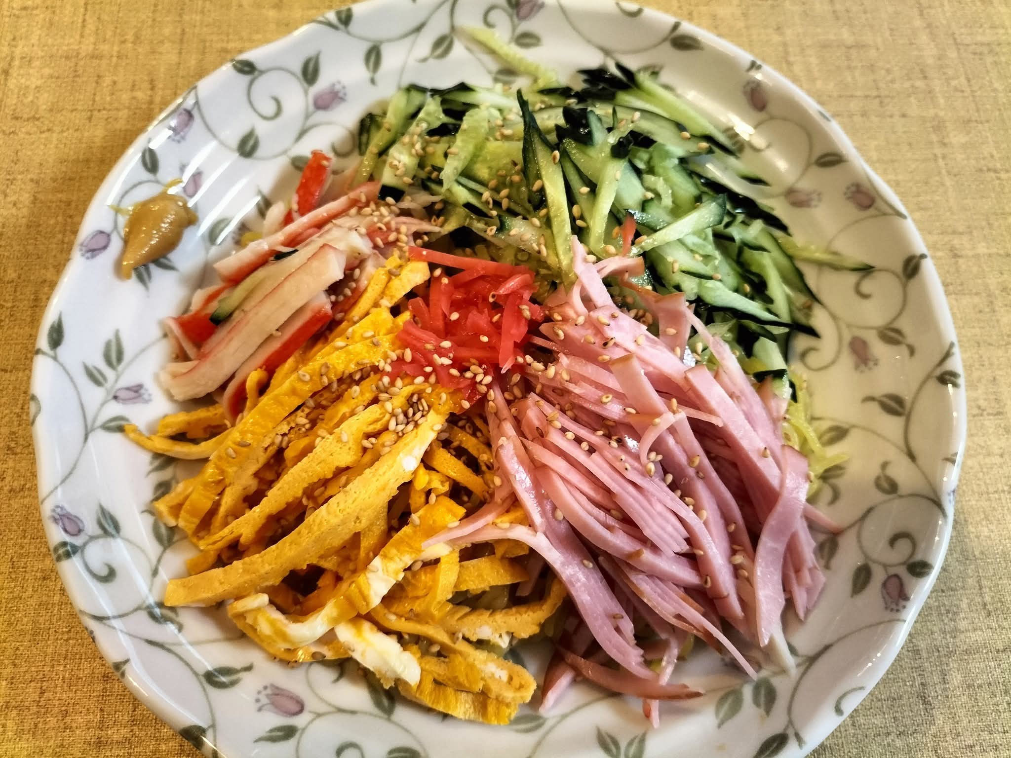 定番具材の錦糸卵、ときゅうり、ハムにカニカマ、ゴマをトッピングした具だくさんの冷やし中華